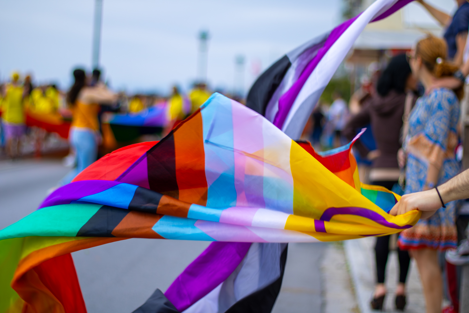 Progressive Pride Flagge im Wind, bunte Menschen verschwommen im Hintergrund